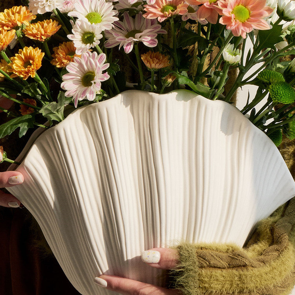 Vase en céramique fait main Moyyudé blanc avec texture ondulée tenu devant des fleurs colorées